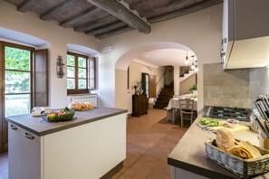 Una cocina con una isla central, un comedor con mesa y sillas, y una escalera que sube a otro nivel.
