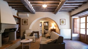 A cozy living room with a fireplace, a sofa, a chair, and a table. There is a window on the right side and an arched doorway leading to another room. - Private Villa with hot tub, A/C, private pool, WIFI, TV, patio, panoramic view, close to Cortona (Terontola)