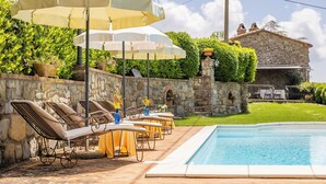 Un espace aménagé au bord de la piscine, avec des chaises longues, des parasols et un mur en pierre.