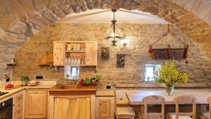 Une cuisine rustique avec des murs en pierre, des meubles en bois, un luminaire suspendu et un coin repas avec des chaises et une table en bois.