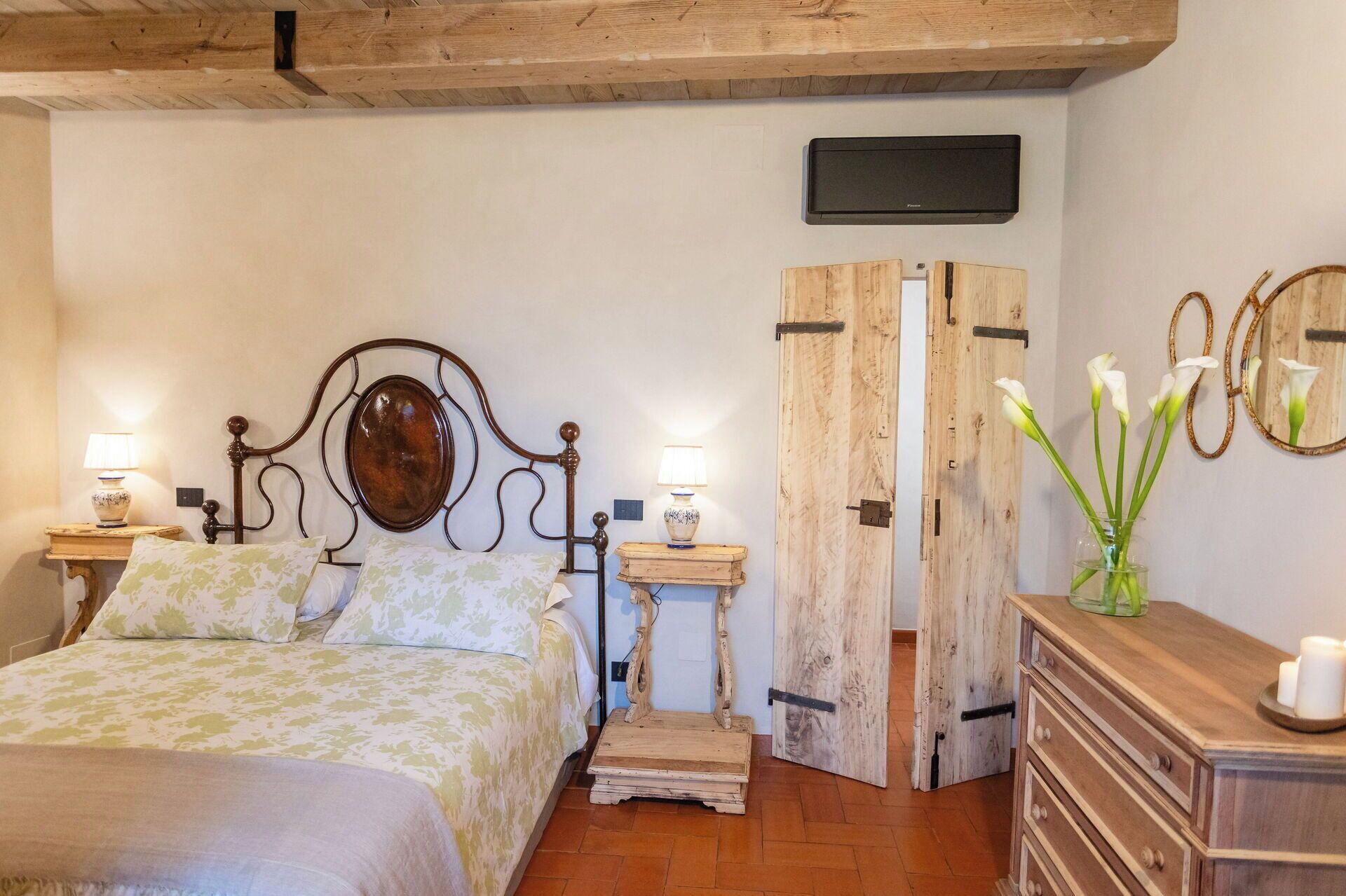 A bedroom with a bed, bedside tables, a TV, a wooden wardrobe, and a dresser.