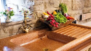 Un évier de cuisine adossé à un mur en pierre, un vase décoratif rempli de fleurs et un plateau en bois contenant des légumes.