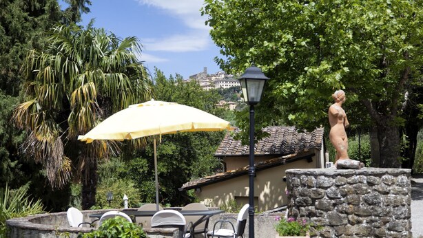 An outdoor patio with stone tables and chairs, a yellow umbrella, and a statue. - Casa Vittoria 1 - Apartment with swimming pool (Cortona)