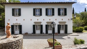 A white building with green shutters, a stone statue, and a lamp post. - Casa Vittoria 1 - Apartment with swimming pool (Cortona)