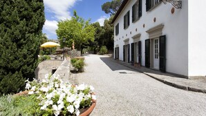 A cobblestone street leading to a white building with black shutters, surrounded by greenery and a stone wall. - Casa Vittoria 1 - Apartment with swimming pool (Cortona)