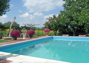 Una piscina con superficie d'acqua cristallina e blu, circondata da piante in vaso e un giardino.