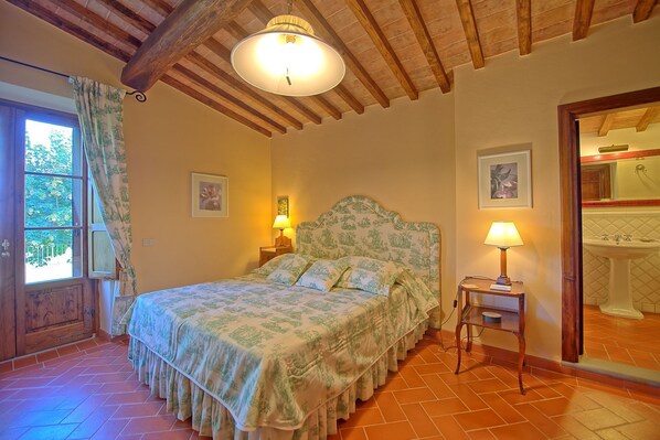 A bedroom with a bed, two bedside lamps, a wooden headboard, and a window with curtains.