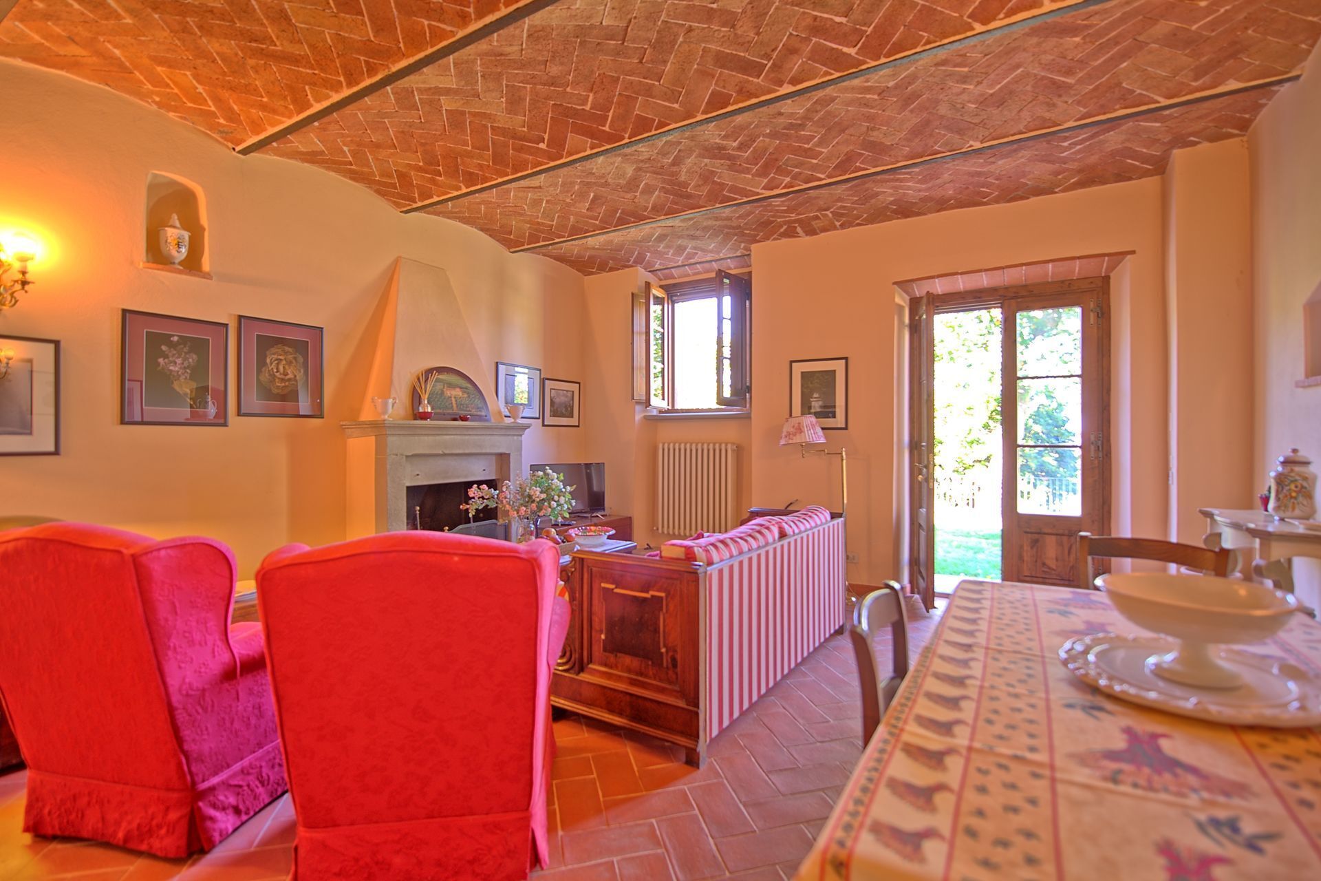 A cozy room with a fireplace, a dining table with a patterned tablecloth, and two red chairs.