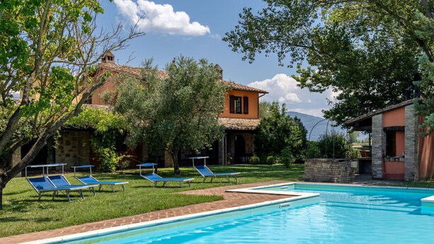 Un'area piscina con lettini e un edificio in pietra con tetto a tegole.