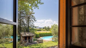 Vista di una piscina, un piccolo edificio in mattoni e una zona erbosa con alberi.
