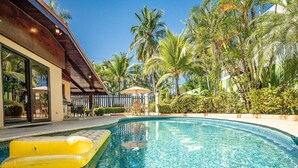 A swimming pool with a yellow inflatable float, surrounded by palm trees and a covered patio area. - Casa Mandolina on the beach in Jaco (Jaco)