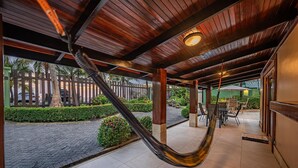 A covered outdoor area with a hammock, tiled flooring, and a view of a paved street and greenery.
