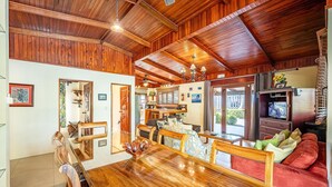 A spacious living area with a wooden ceiling, a dining table, and a red sofa.