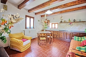 A cozy living room with a sofa, a dining table, and a kitchen area with wooden cabinets and a tiled backsplash.