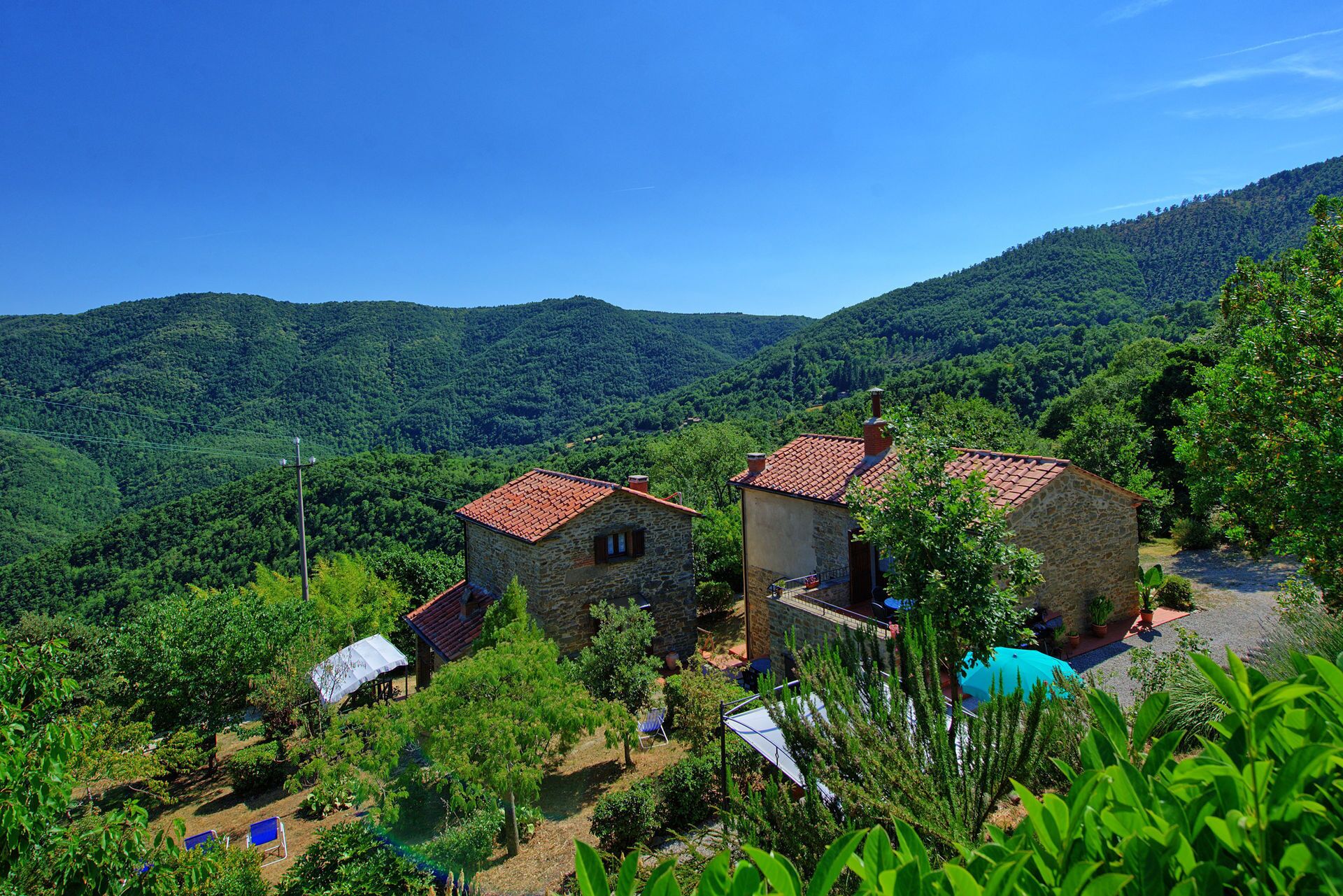 A stone building with a red-tiled roof, surrounded by lush greenery and hills.