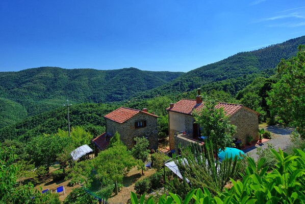 A stone building with a red-tiled roof, surrounded by lush greenery and hills.