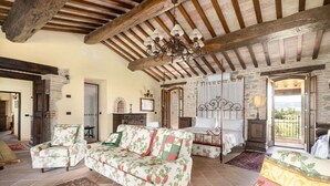 A rustic room with exposed wooden beams, a floral sofa, a bed with a canopy, and a view through a window.