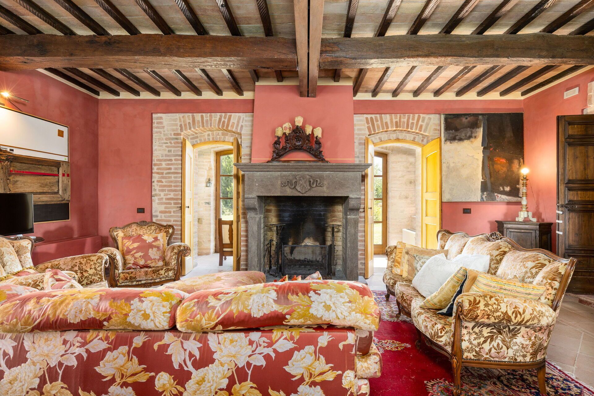 A room with a fireplace, floral upholstery, and a red carpet.