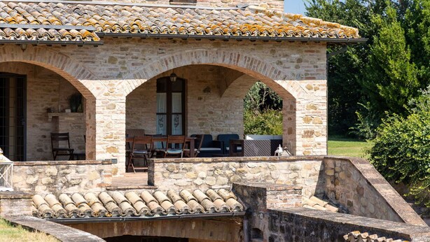 A stone building with a tiled roof, a covered patio with seating, and a small water feature.