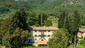 Un bâtiment à deux étages, doté d’un toit en tuiles, entouré d’une végétation luxuriante et avec des montagnes en arrière-plan.