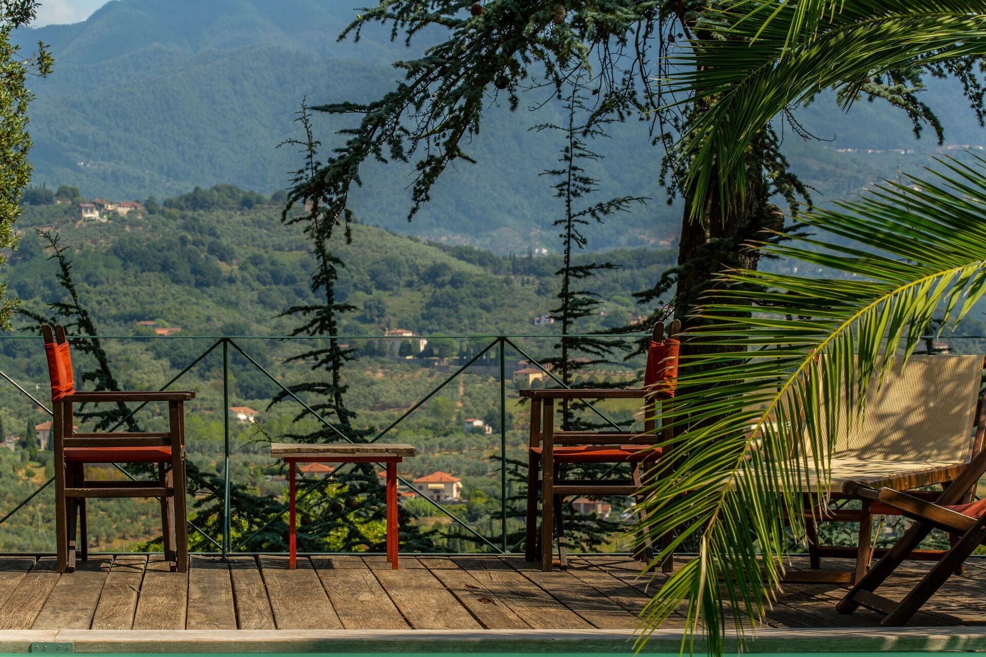 Terraza de madera con sillas y una mesa, con vistas a un paisaje montañoso.