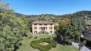 Un edificio grande de dos pisos con techo de tejas, rodeado de jardines y árboles bien cuidados.