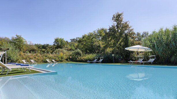 Una piscina cristalina con sillas de descanso y sombrillas, rodeada de exuberante vegetación.