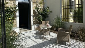 Un patio con mesa y sillas, rodeado de plantas y un muro de piedra.