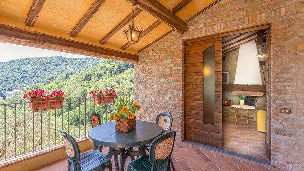 Un balcón con una mesa y sillas, un farol colgante y vistas a un paisaje montañoso.