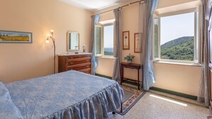 Un dormitorio con cama, cómoda, tocador y ventanas grandes con cortinas.