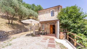 Una casa de piedra con puerta de madera, un pequeño patio con mesa y sillas, y un muro de piedra.