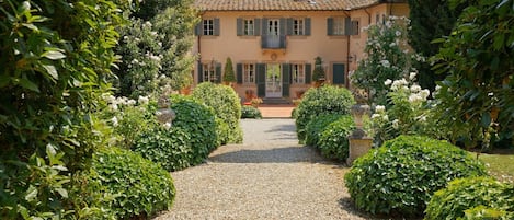 Eine Villa mit einem Kiesweg, der zu einer Haustür führt, umgeben von üppigem Grün und weißen Blüten.