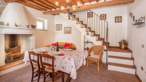 Zona pranzo con tavolo apparecchiato per quattro persone, camino e una scala che conduce al piano superiore.