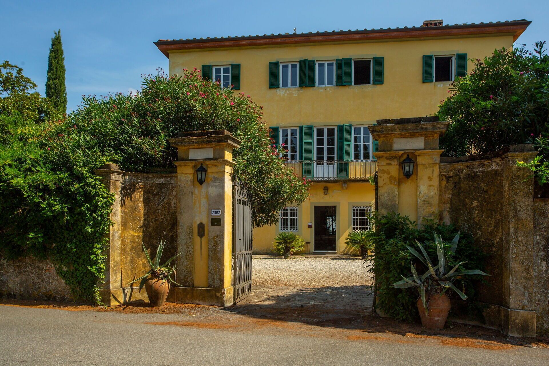 A yellow building with green shutters, a gated entrance, and potted plants.