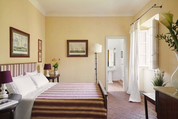 A hotel room with a bed, a nightstand, a lamp, a vase with flowers, and framed pictures on the wall.