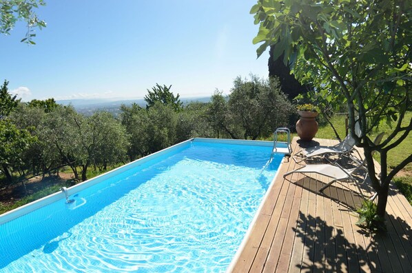 Uma piscina retangular com águas cristalinas azuis, rodeada por um deck de madeira e vegetação exuberante.
