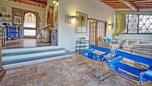 A spacious living area with a stone fireplace, a blue sofa set, and a wooden ceiling. - Beautiful apartment for 2 guests with pool, A/C, WIFI, TV and panoramic view (San Gimignano)