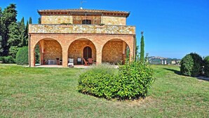 Un edificio de piedra con tres arcos, un pequeño jardín y vistas a un pueblo lejano.
