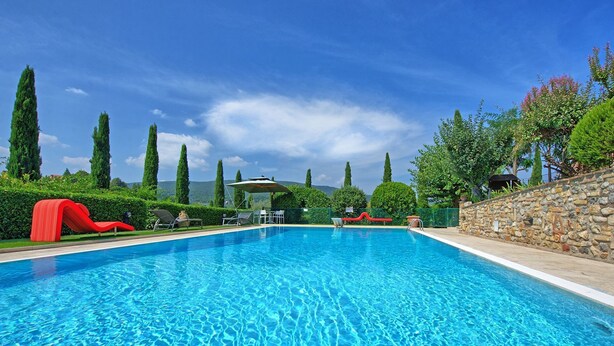 Una piscina con acqua cristallina blu, circondata da vegetazione e muri in pietra.