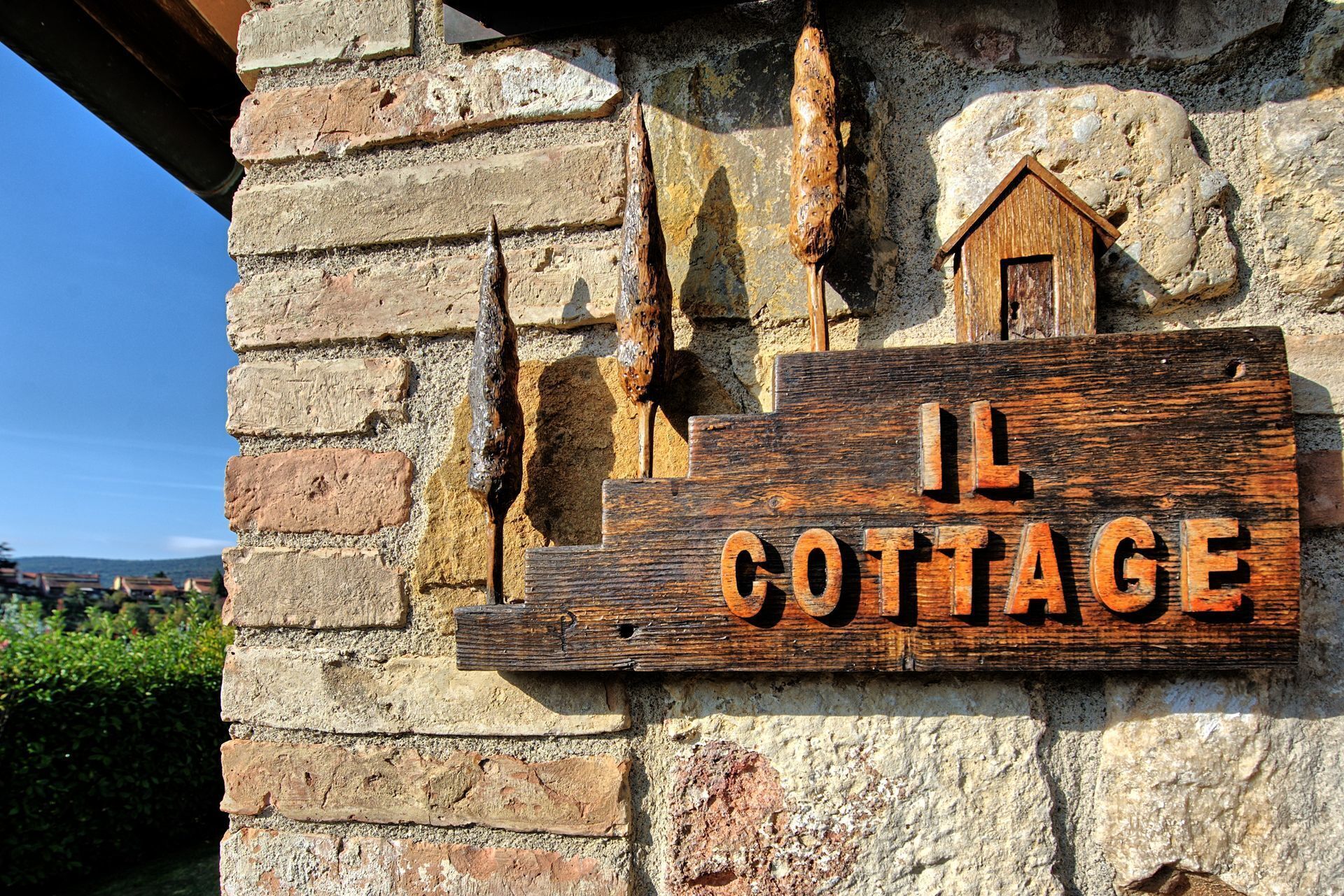 Une enseigne en bois rustique portant l’inscription « IL COTTAGE », fixée à un mur de pierre.