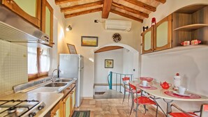 A kitchen with a gas stove, sink, and a refrigerator. There is a dining area with red chairs and a table. - Nice apartment for 2 guests with A/C, WIFI, pool, TV and panoramic view (San Gimignano)