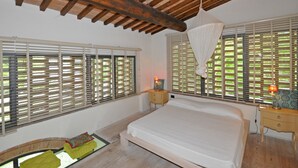Un dormitorio con una cama grande, vigas de techo de madera y ventanas con persianas.