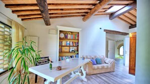 Una sala de estar acogedora con techo de madera, una estantería llena de libros, una mesa de comedor y un sofá.