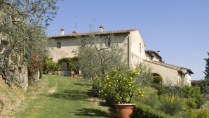 Una casa rustica con tetto spiovente, circondata da un giardino curato con piante in vaso e un prato.