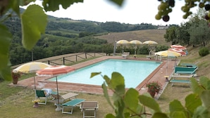 Ein rechteckiger Pool mit umlaufender Liegefläche, ausgestattet mit mehreren Sonnenschirmen und Liegestühlen.