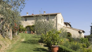 A rustic house with a sloped roof, surrounded by a well-maintained garden with potted plants and a lawn. - Cosy apartment for 3 people with pool, A/C, WIFI, pets allowed and panoramic view (San Gimignano)