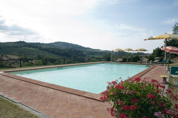 Una piscina con vistas a colinas, rodeada de sillas de descanso y sombrillas.