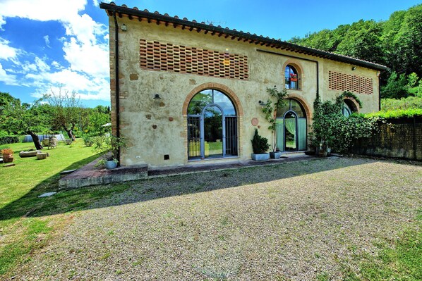 A rustic building with a gravel driveway, arched windows, and a tiled roof.