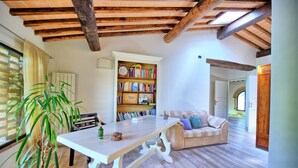 Een gezellige woonkamer met een houten plafond, een boekenplank vol boeken, een eettafel en een bank.