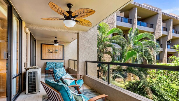 Ein Balkon mit Deckenventilator, Klimaanlage und Holzstühlen mit gemusterten Kissen.